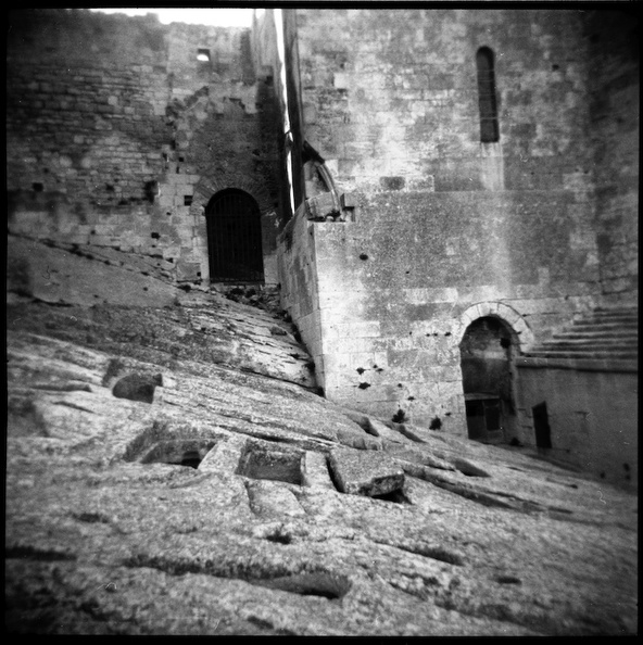 Abbaye de Montmajour: tombes dans la pierre. Hogla 120CFN. 320 Tri-X - Les tombes qui entourent l'abbaye sont creusées comme des baignoires funèbres dans la roche bleue, avec un coussinet de pierre pour soutenir la nuque du défunt. l"es plus petites ne sont pas, comme on l'a cru, des tombes d'enfants, mais des réceptacles où l'on recueillait, pêle-mêle, les restes épars des morts les plus anciens. Deux de ces tombes, sous le portique de la chapelle, symboliseraient l'une la mort, l'autre la nature. Creusé lui aussi dans le roc, une sorte de siège vous sera désigné comme le confessional de saint Trophime, c'est-à-dire la cellule de cet ermite qui, dit-on, se serait réfugié à Montmajour au temps de la persécution. img012rez.jpg